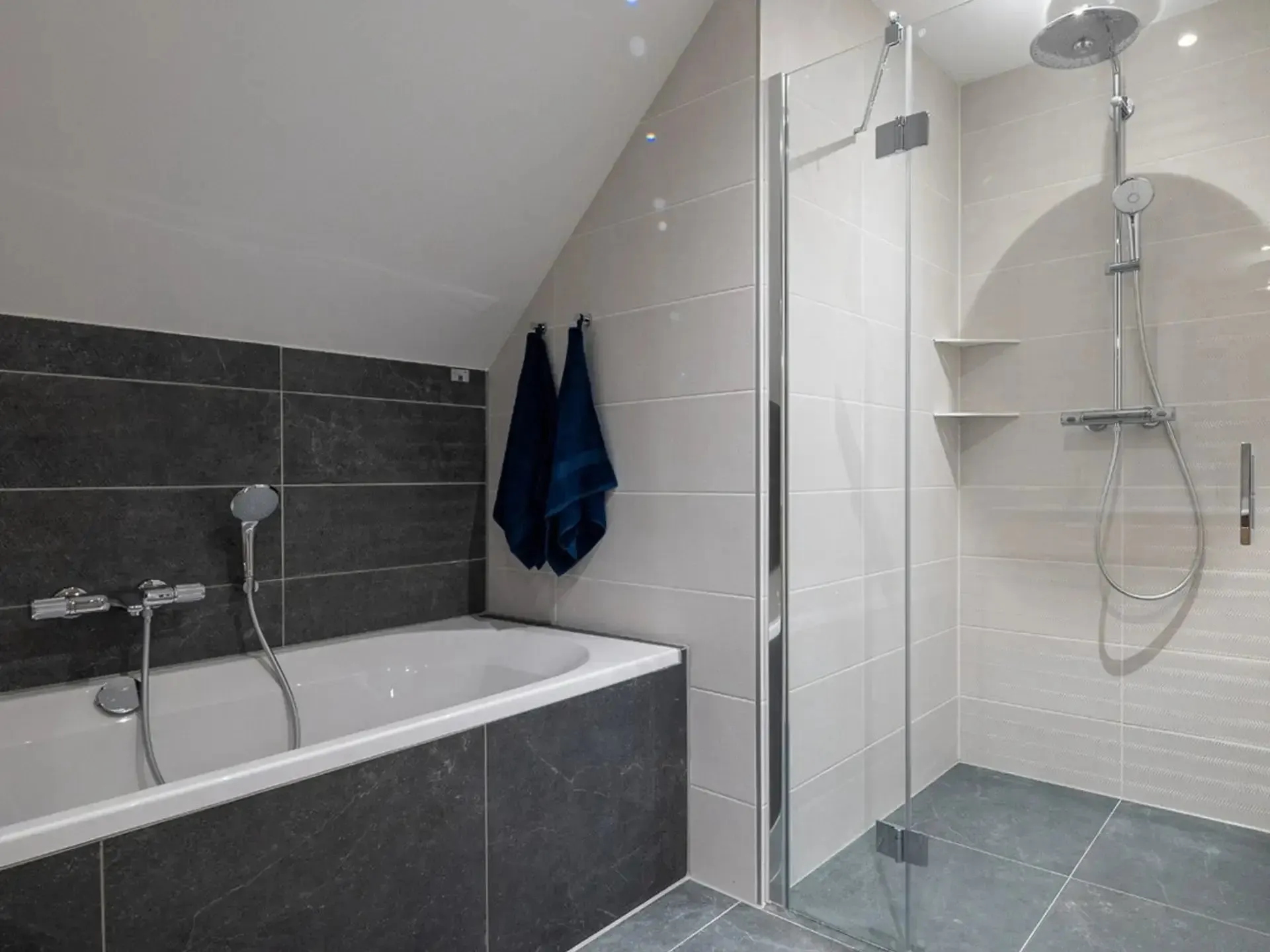 Badkamer onder een schuin dak met ligbad en inloopdouche