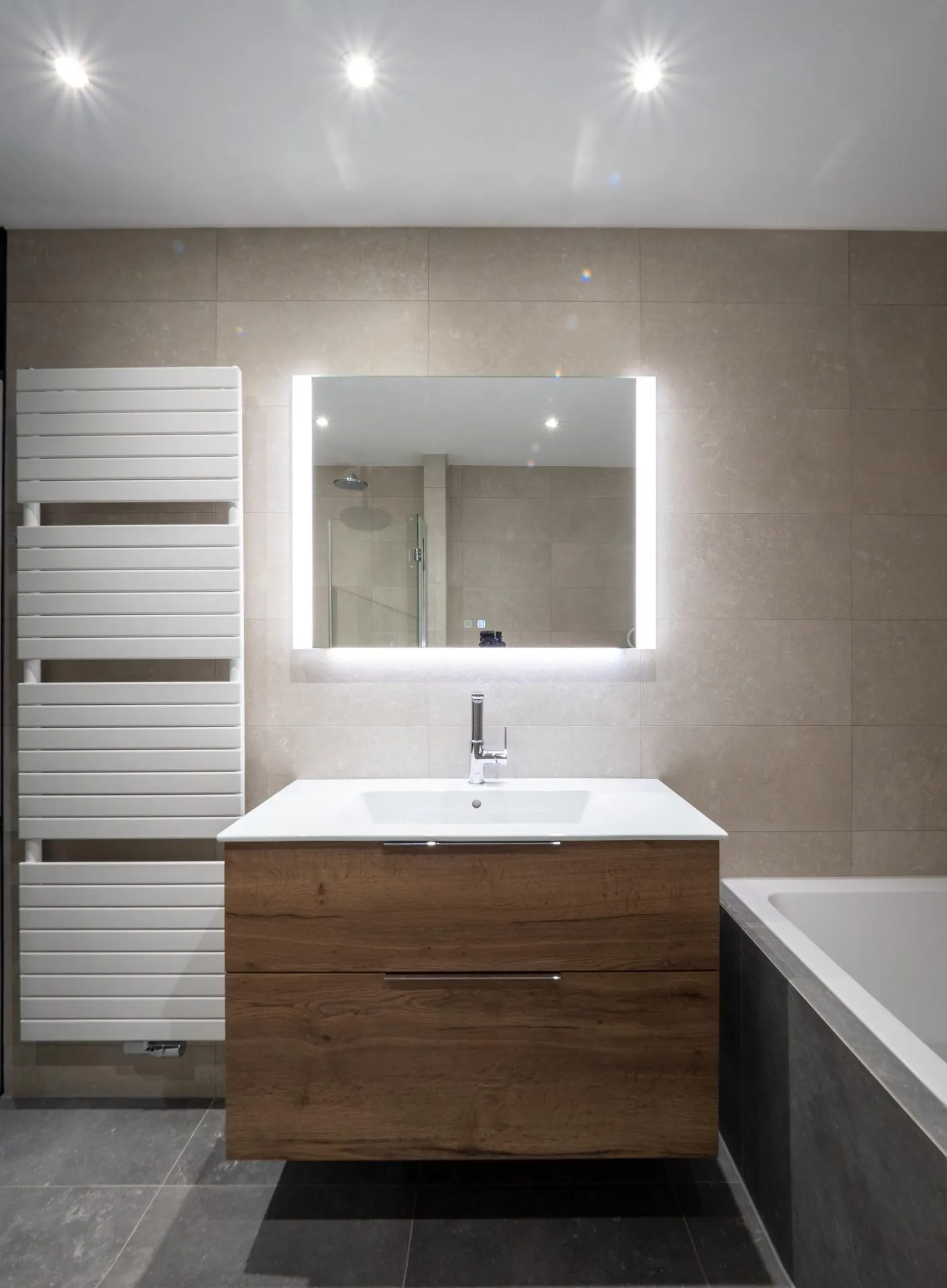 Badkamer met houten wastafelmeubel, verlichte spiegel en ligbad