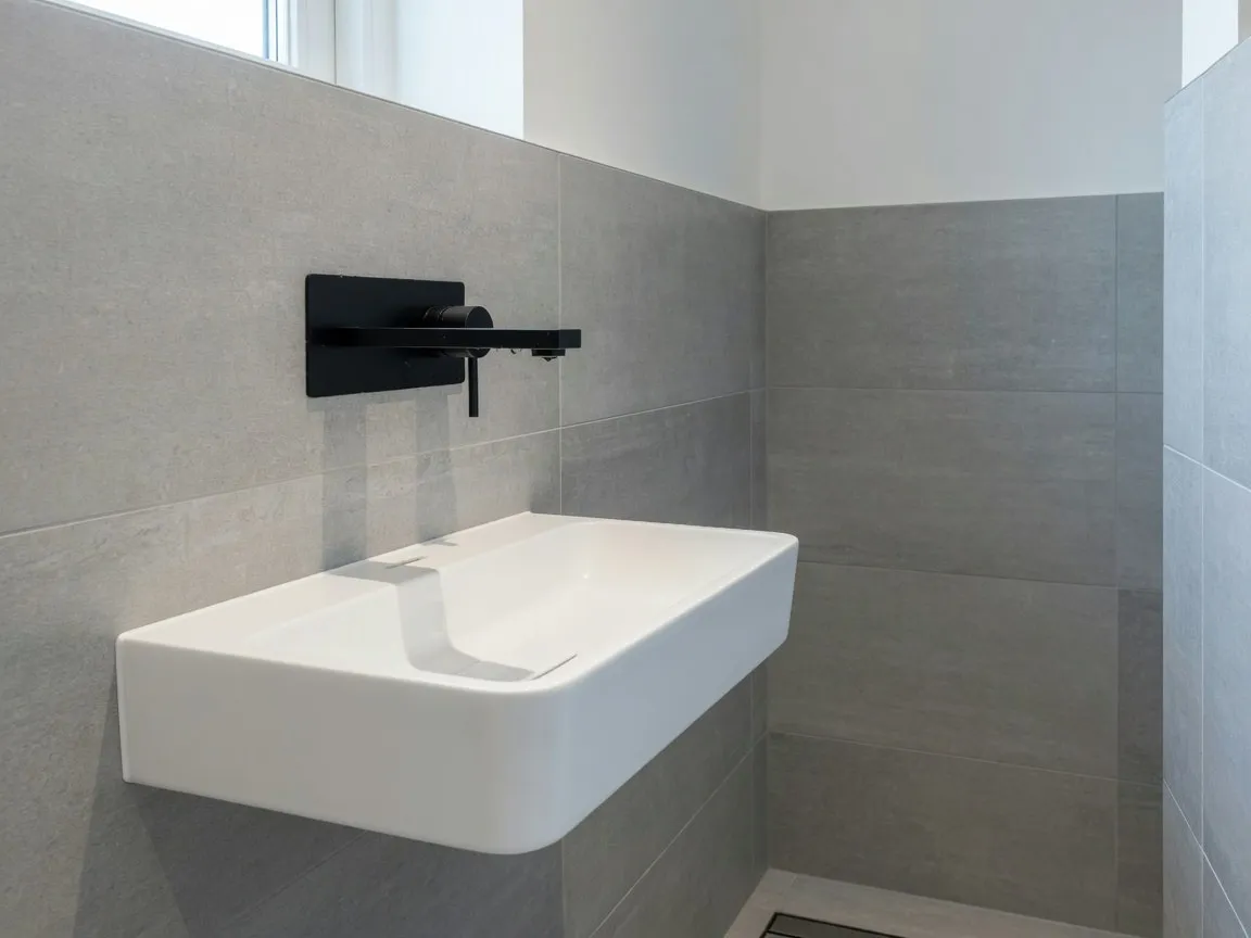 Detail van een moderne badkamer met zwarte wandkraan boven een slanke witte wastafel